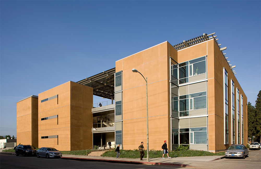 Image 2. Corner view of a 3-story terra cotta-colored modern building with large glass windows.