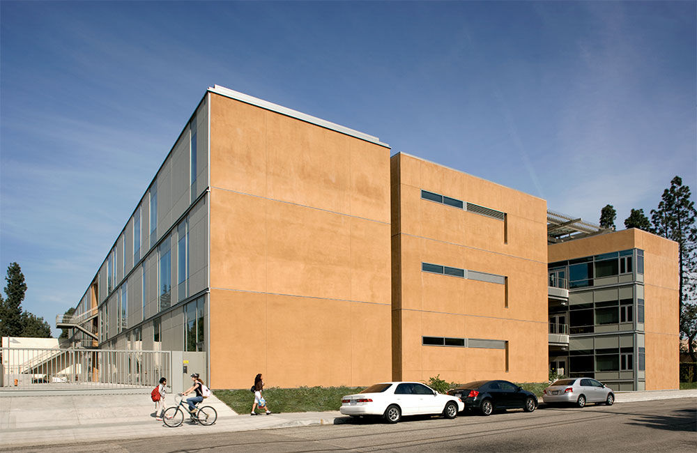 Image 4. Side view of a 3-story terra cotta-colored modern building with large glass windows.