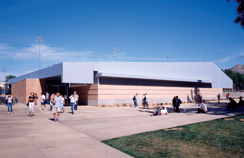Image 5. A 1-story modern sandstone-colored building with angular light grey metal roof.