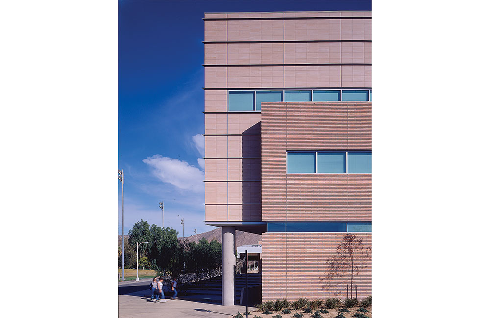 Image 6. Corner view of a 3-story modern building clad with sandstone-colored bricks and tiles.