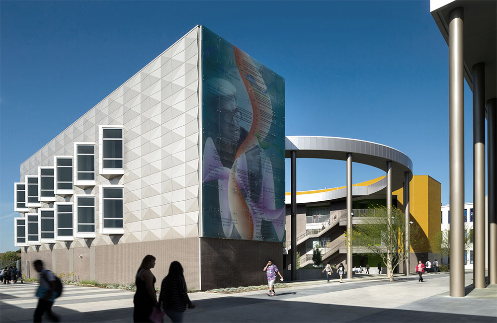 Image 2. Corner exterior back view of 3-story modern building with a series of vertical angled window slots running along the left facade while a circular outdoor courtyard can be seen on the right.