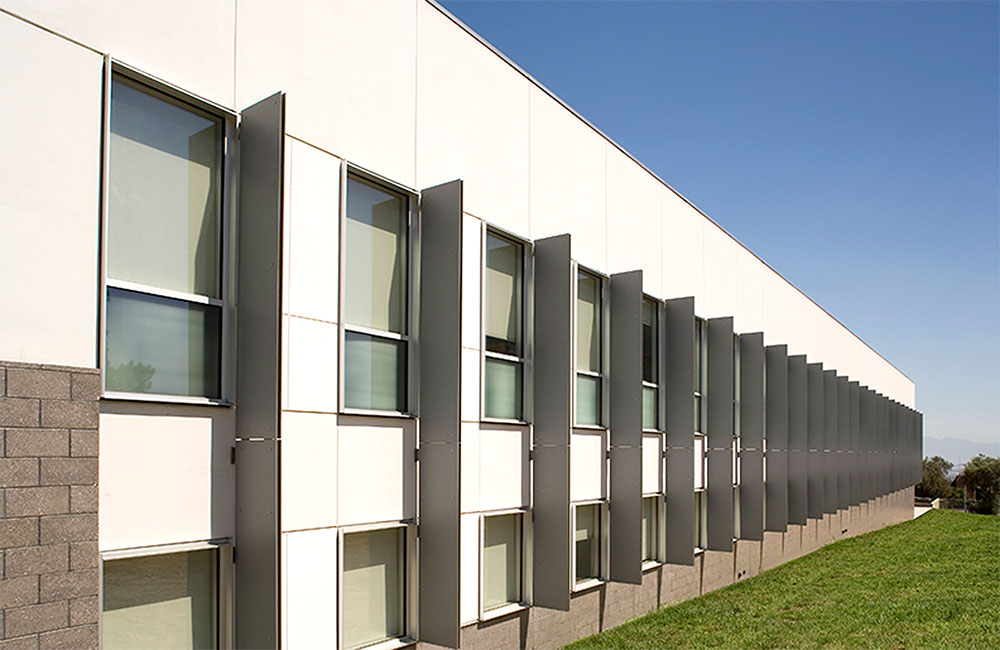 Image 5. Exterior view of modern white and beige building facade punctuated by evenly spaced rectangular windows and vertical sunshade panels.